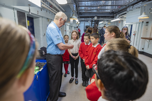 member of museum staff explaining something to a group of attentive youngsters
